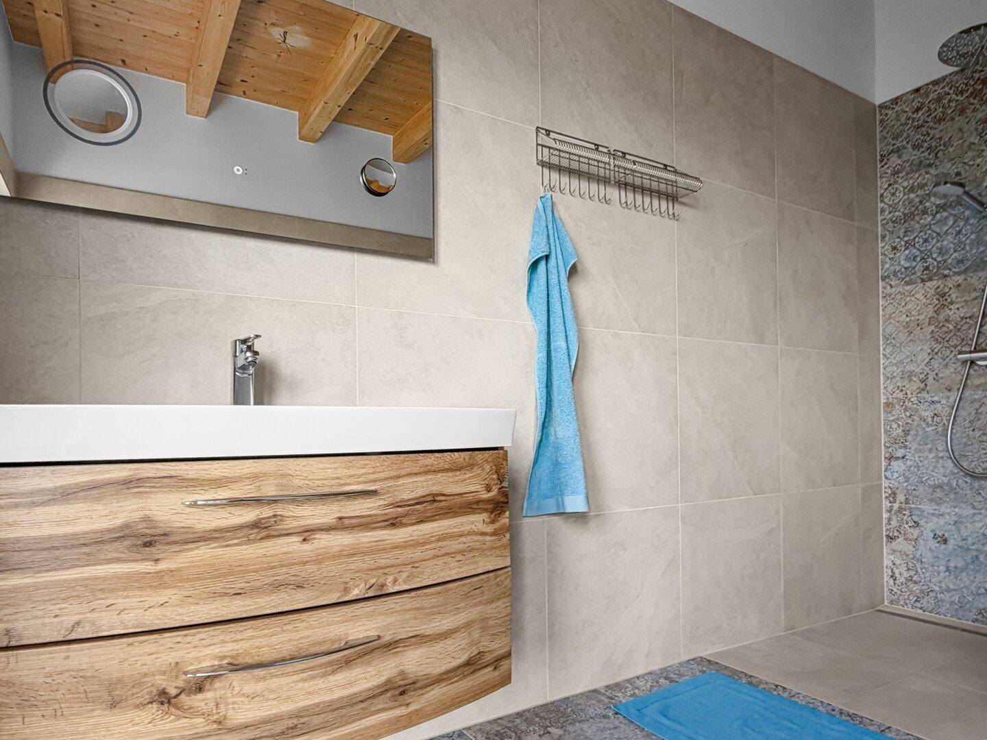 Waschtisch mit Holzunterschrank und Spiegel in einem modernen Badezimmer mit Dusche.