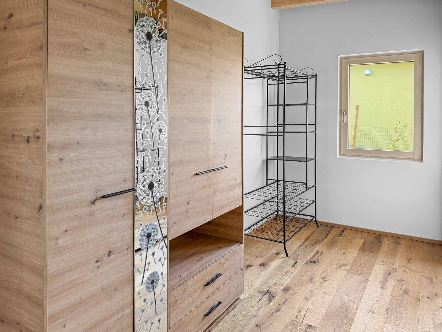 Schlafzimmer mit großem Holzschrank, Holzboden und Fenster mit Blick nach draußen.