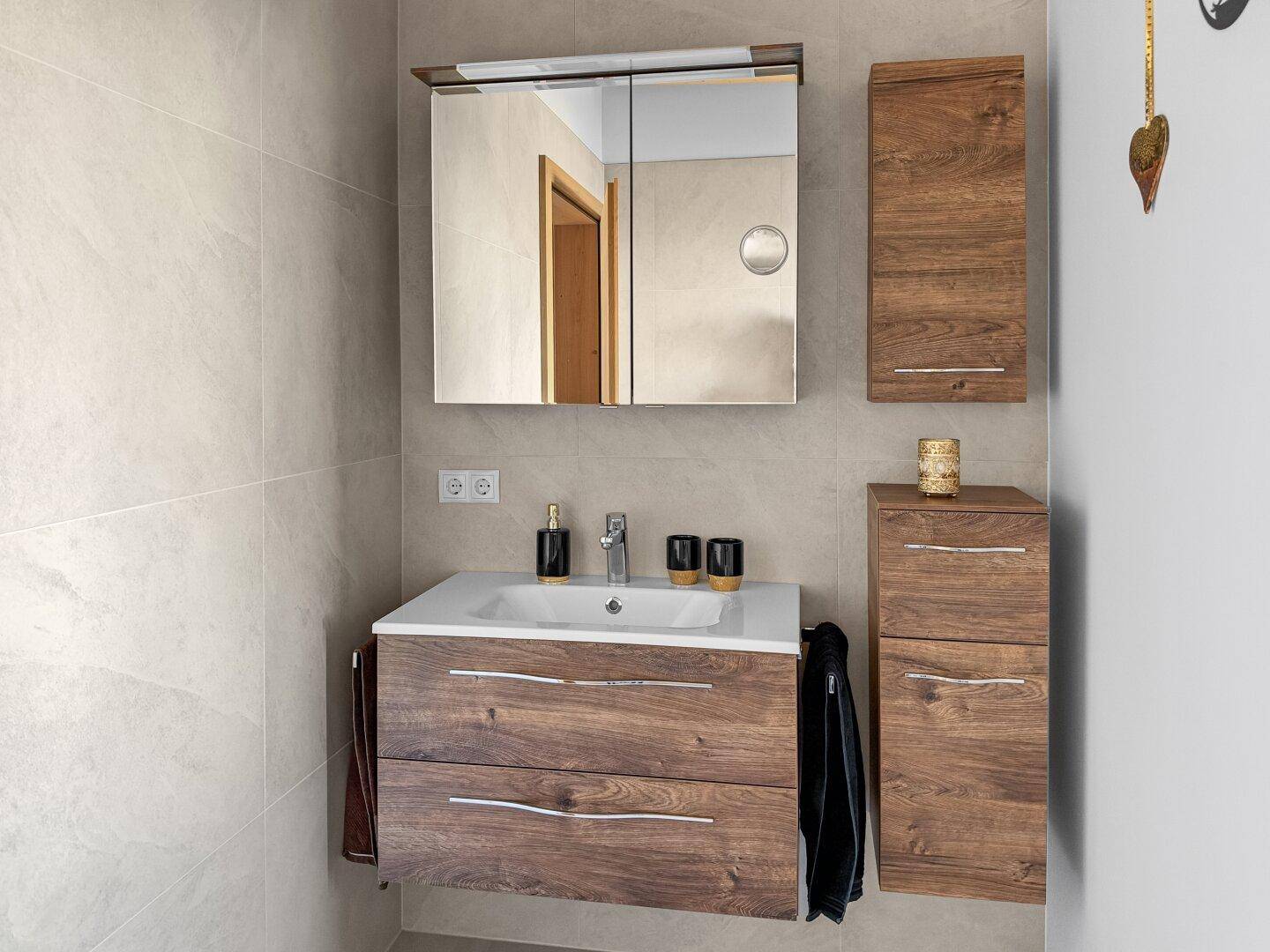 Modernes Badezimmer mit Holzwaschtisch, Spiegelschrank und hellen Fliesen.
