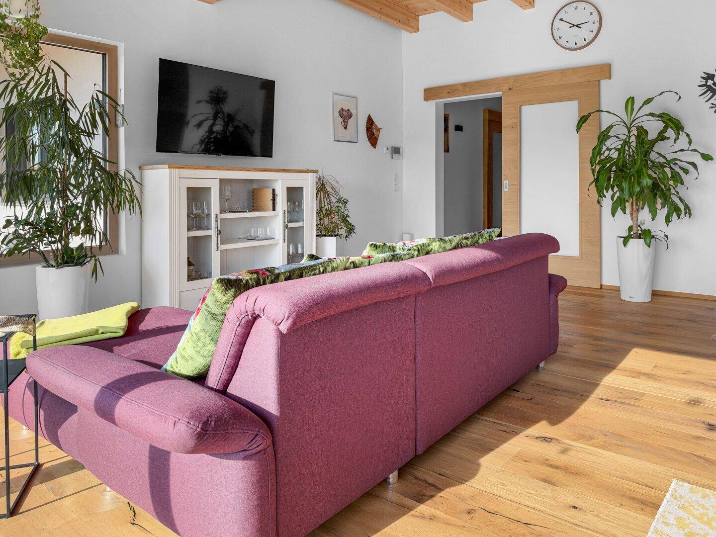 Helles Wohnzimmer mit bequemer Couch, Holzboden und Blick auf die grüne Umgebung durch große Fenster.