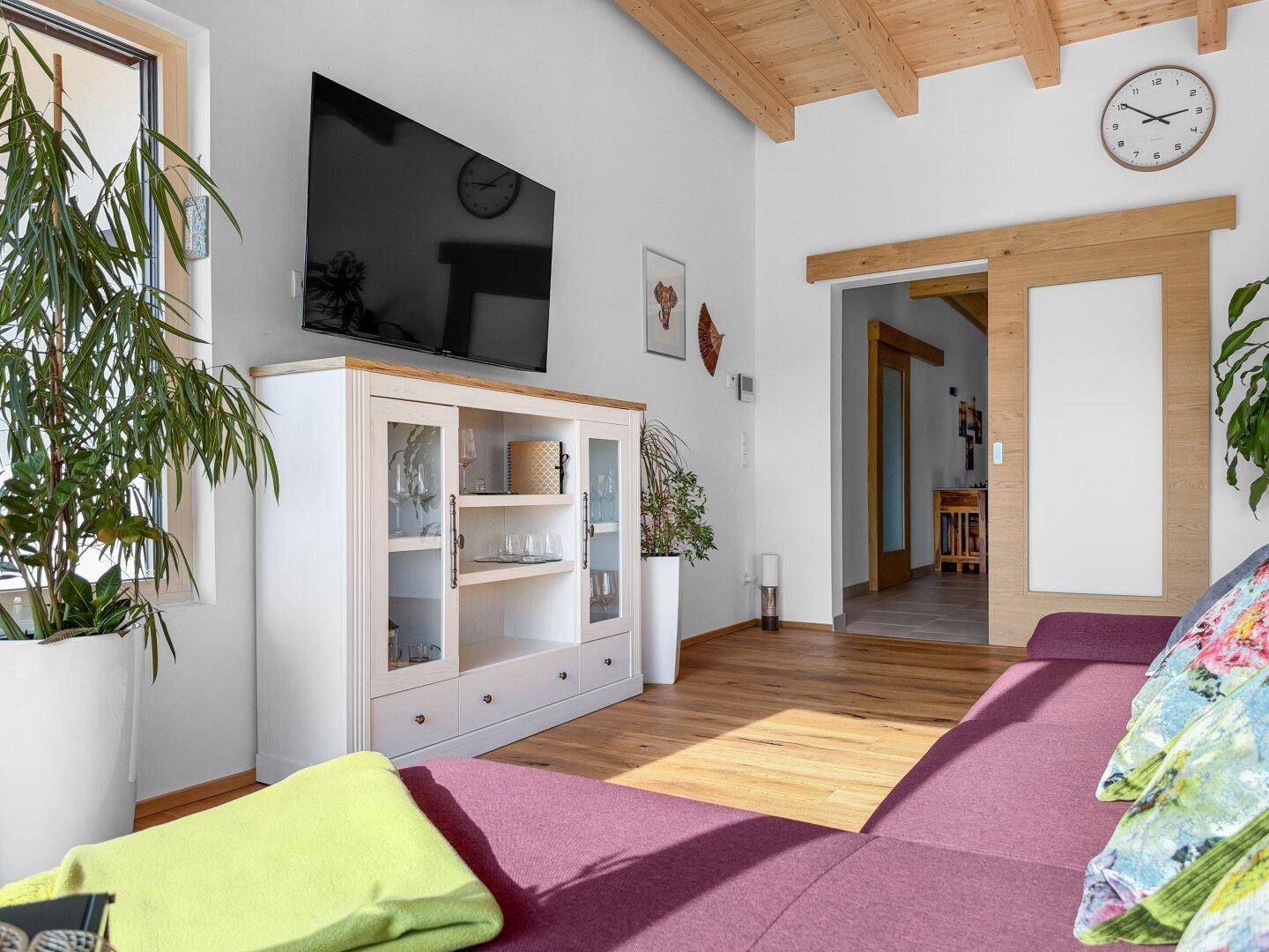Gemütliches Wohnzimmer mit großem Sofa, Fernseher und Holzboden unter einer Holzbalkendecke.