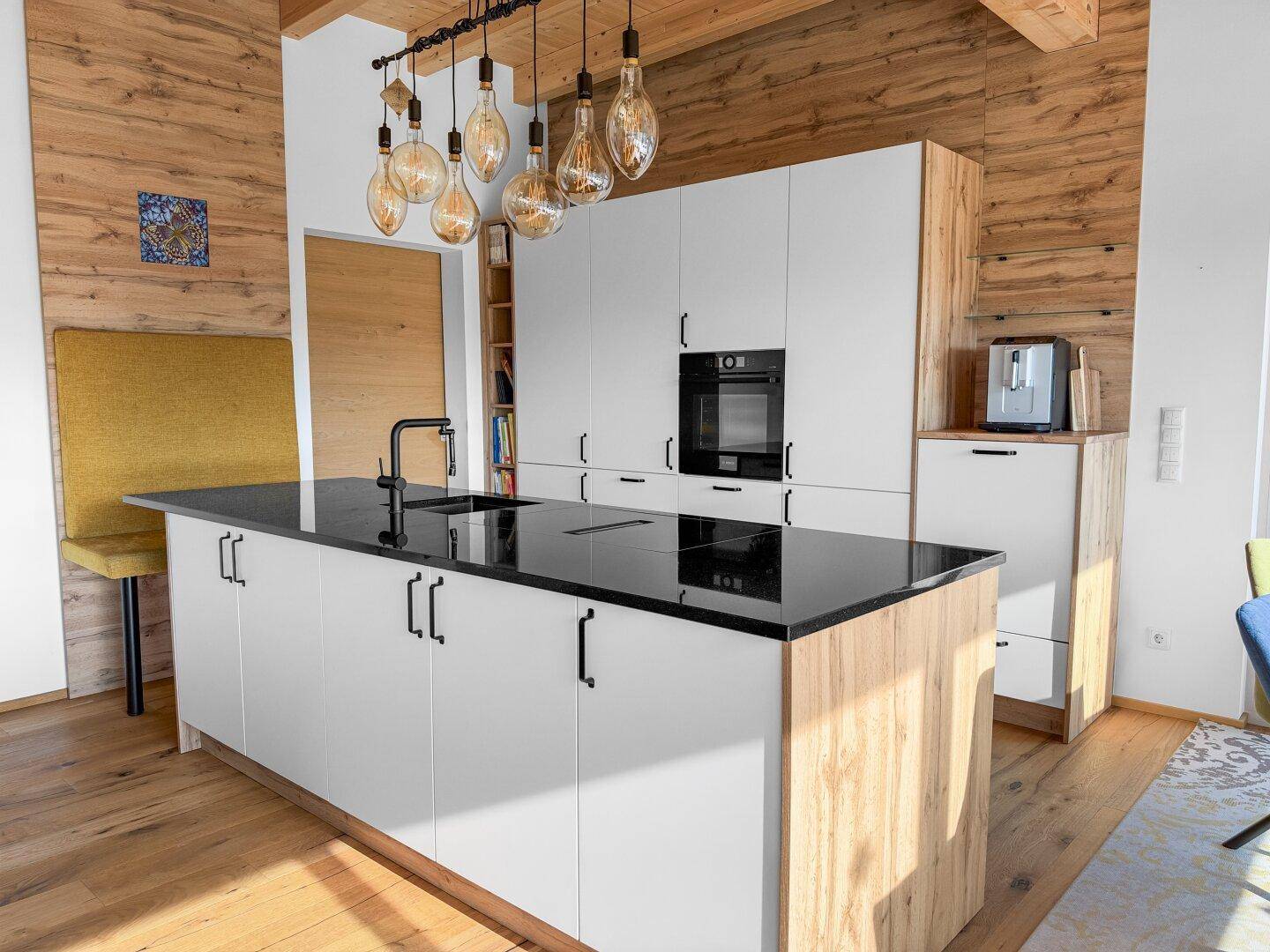Geräumige Küche mit Kochinsel, schwarzen Arbeitsplatten und modernen Einbauschränken unter Holzbalkendecke.