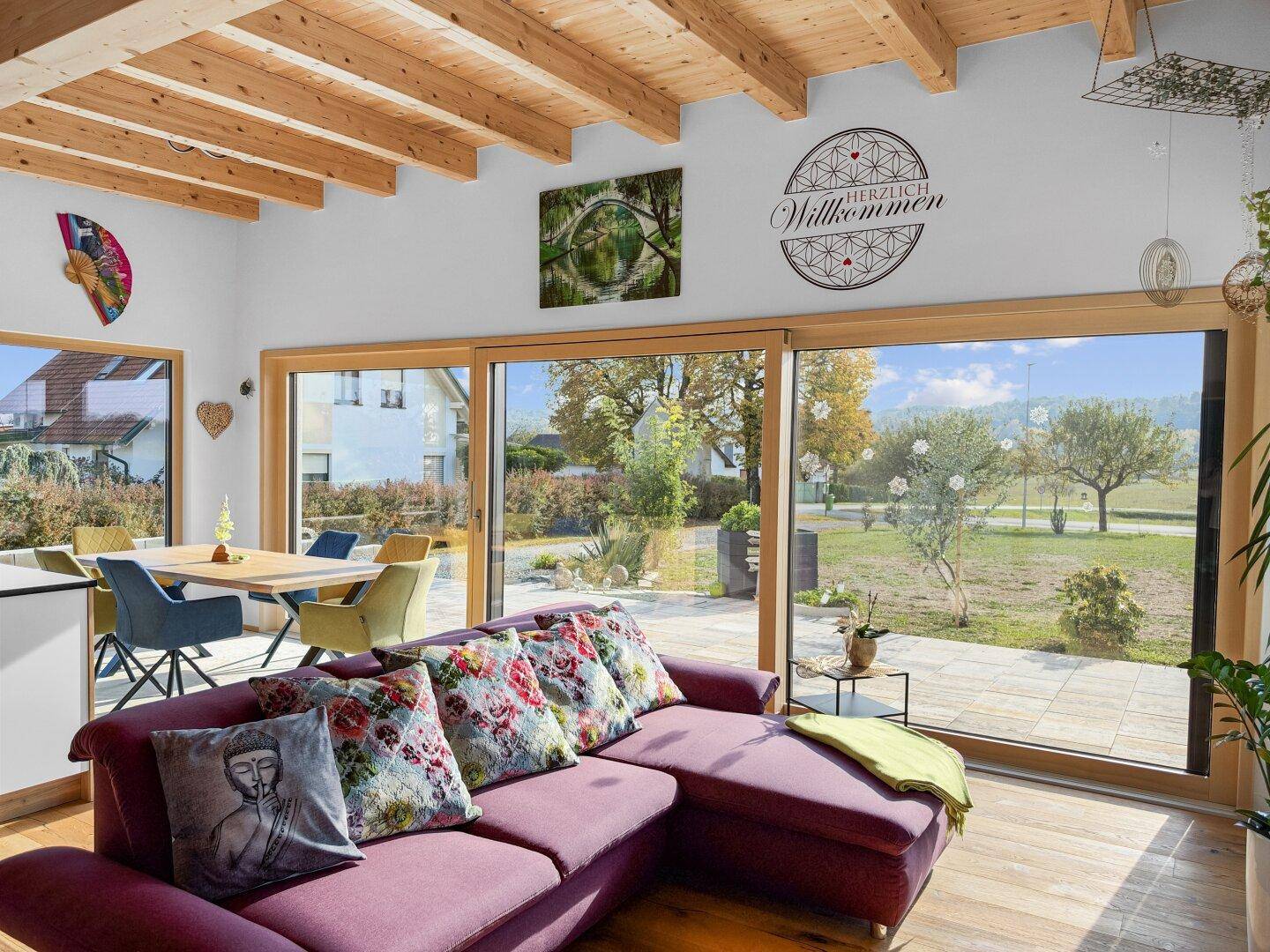 Gemütlicher Wohnbereich mit großer Fensterfront, Holzbalkendecke und Zugang zur Terrasse.