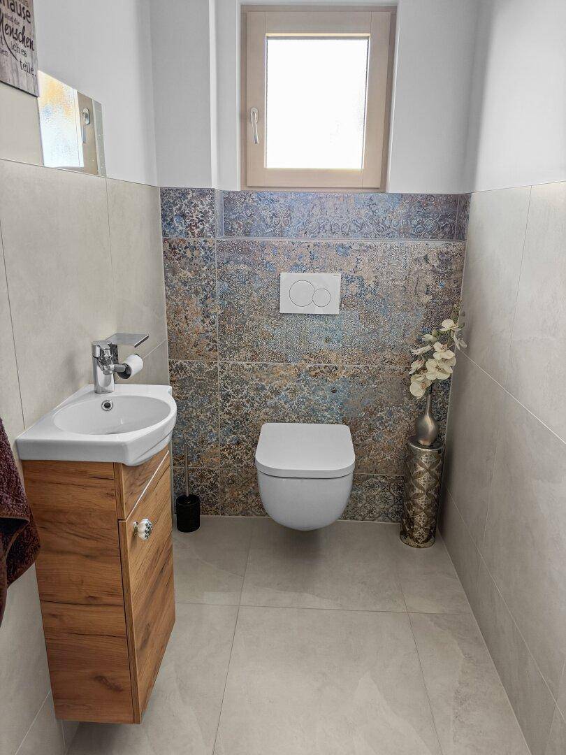 Modernes Gäste-WC mit Wand-WC, kleinem Waschbecken und dekorativen Fliesen.