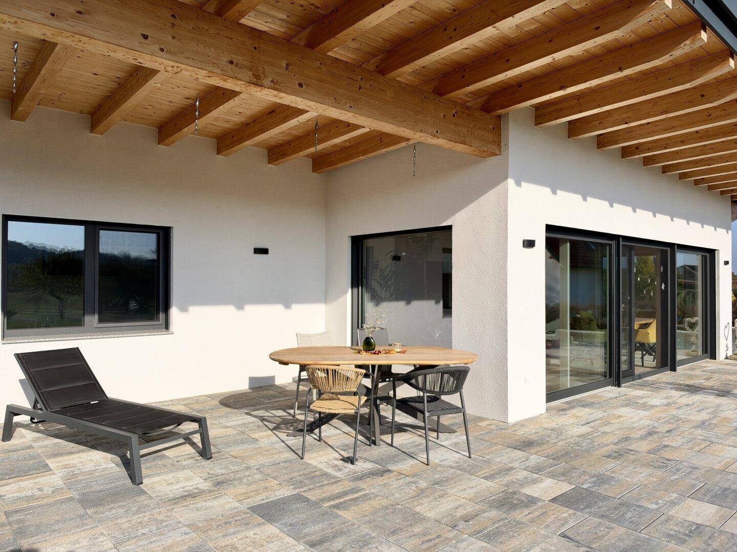 Geräumige Terrasse mit Holzbalkenüberdachung, Fliesenboden und Gartenmöbeln für entspannte Stunden.