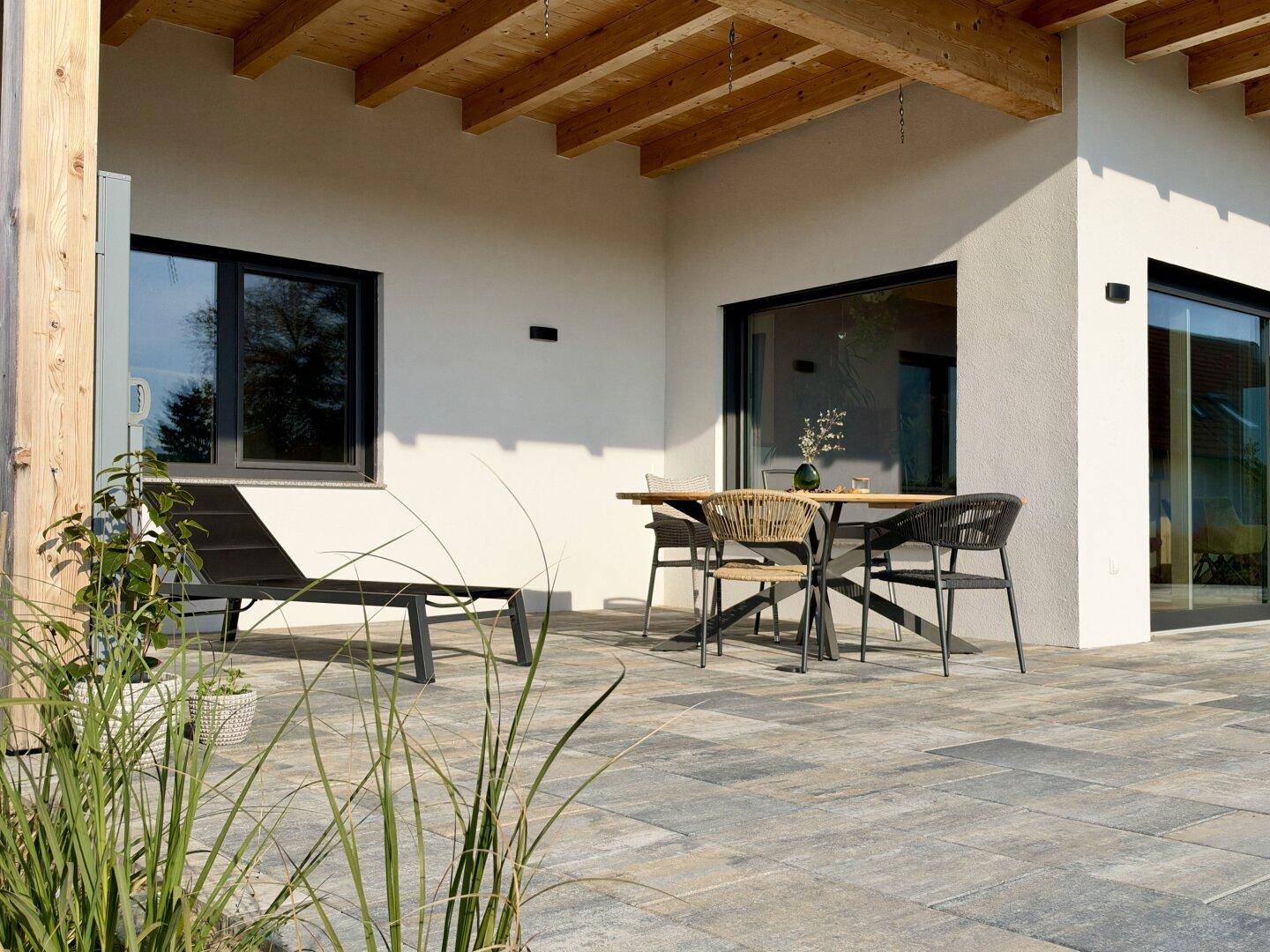 Gemütliche, gepflasterte Terrasse mit modernen Gartenmöbeln und Blick auf die grüne Umgebung.