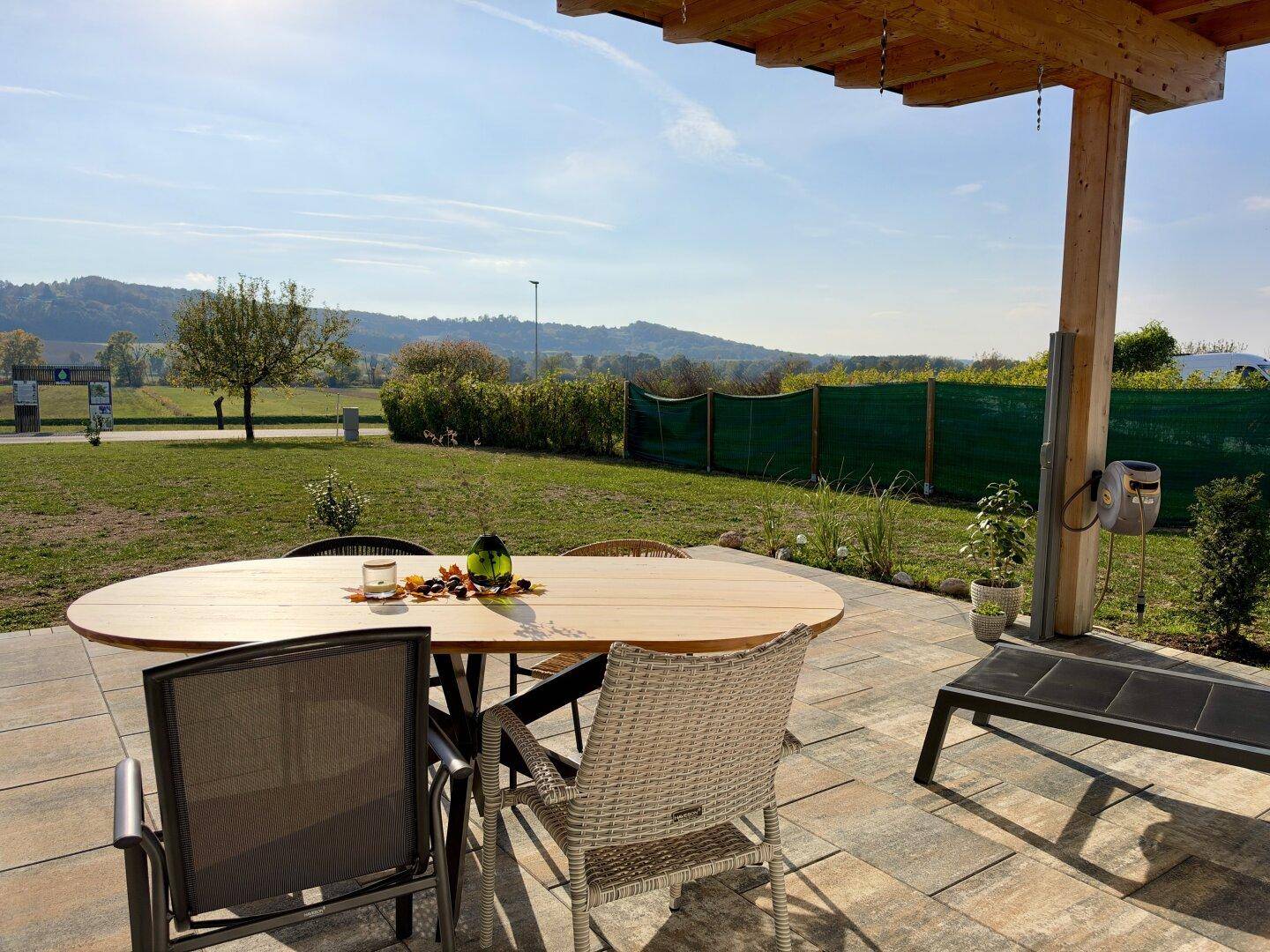 Sonniger Terrassenbereich mit Esstisch und weitem Blick ins Grüne und auf die Landschaft.