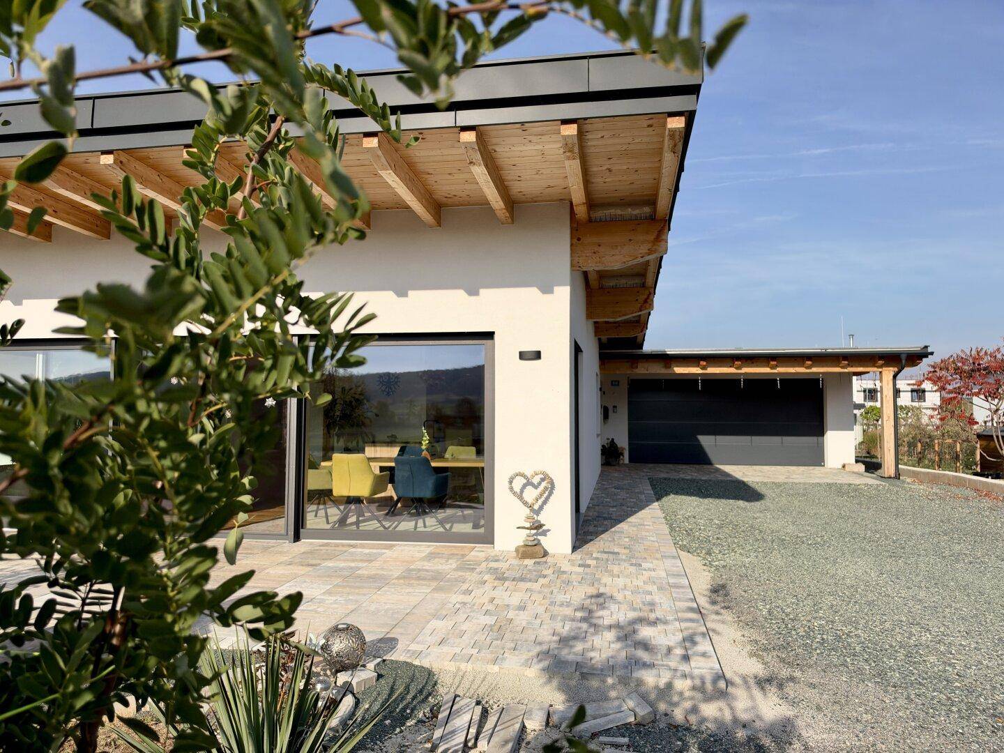 Modernes Einfamilienhaus mit integrierter Garage, Carport und gepflastertem Zugangsbereich.