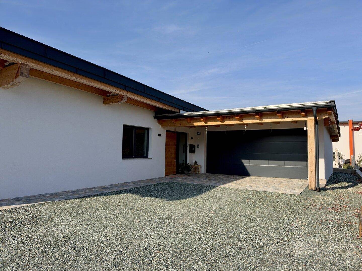 Vorderansicht des modernen Hauses mit integrierter Garage, Carport und Schotterauffahrt.