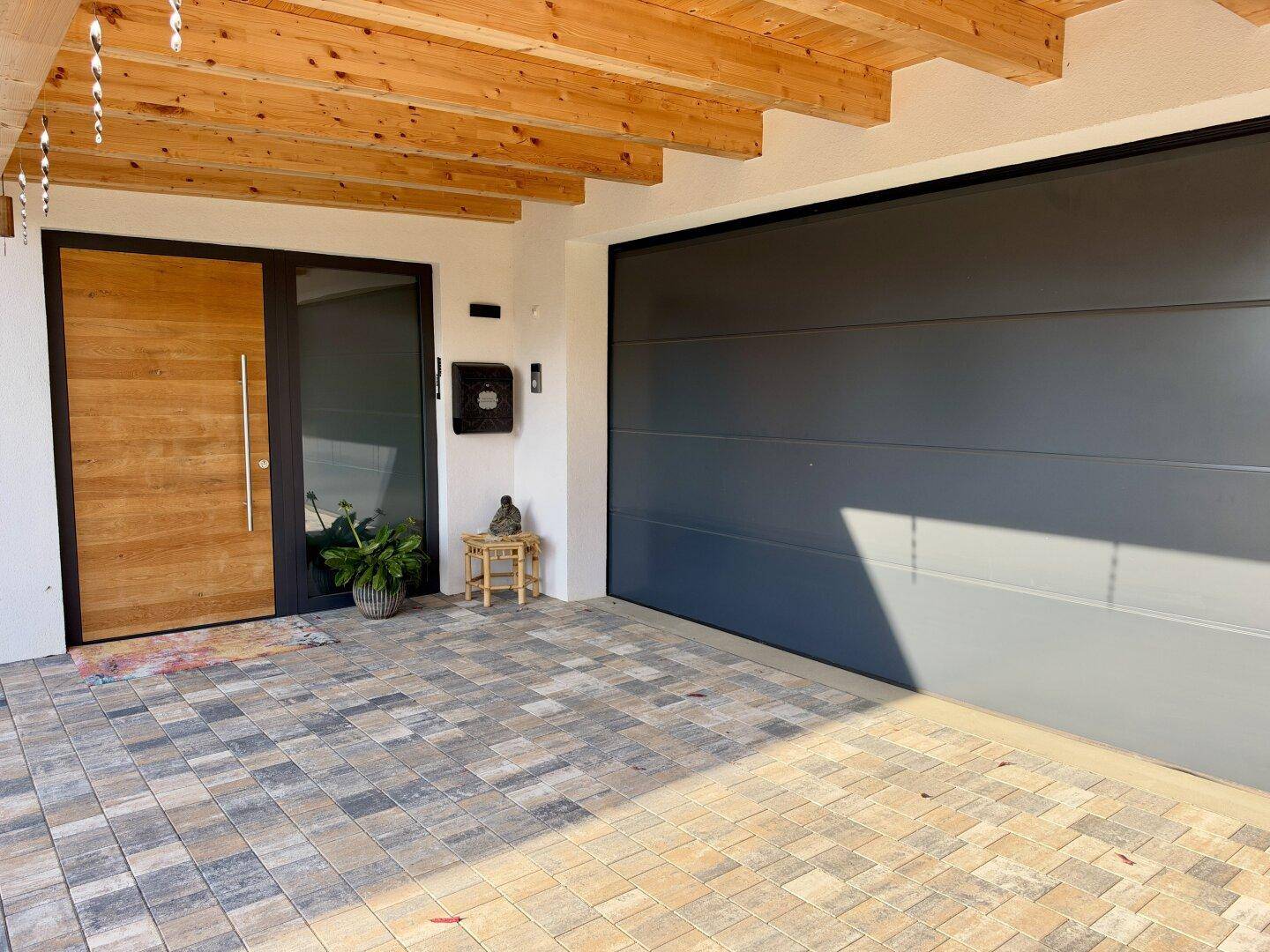 Überdachter Eingangsbereich mit Carport, Garagentor und gepflastertem Vorplatz.