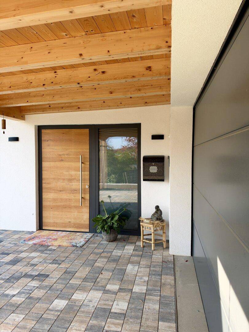 Moderner Hauseingang mit Holztür, gepflastertem Bereich und einem Briefkasten neben der Garage.