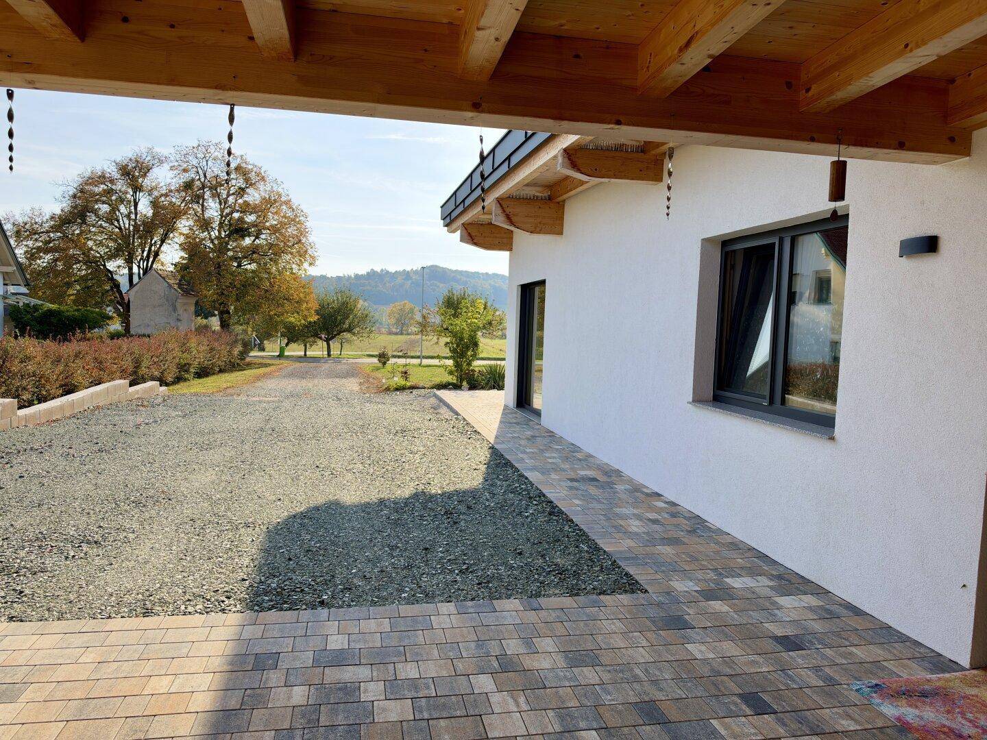 Seitenansicht des Hauses mit gepflastertem Weg, Schotterauffahrt und Blick in die Landschaft.
