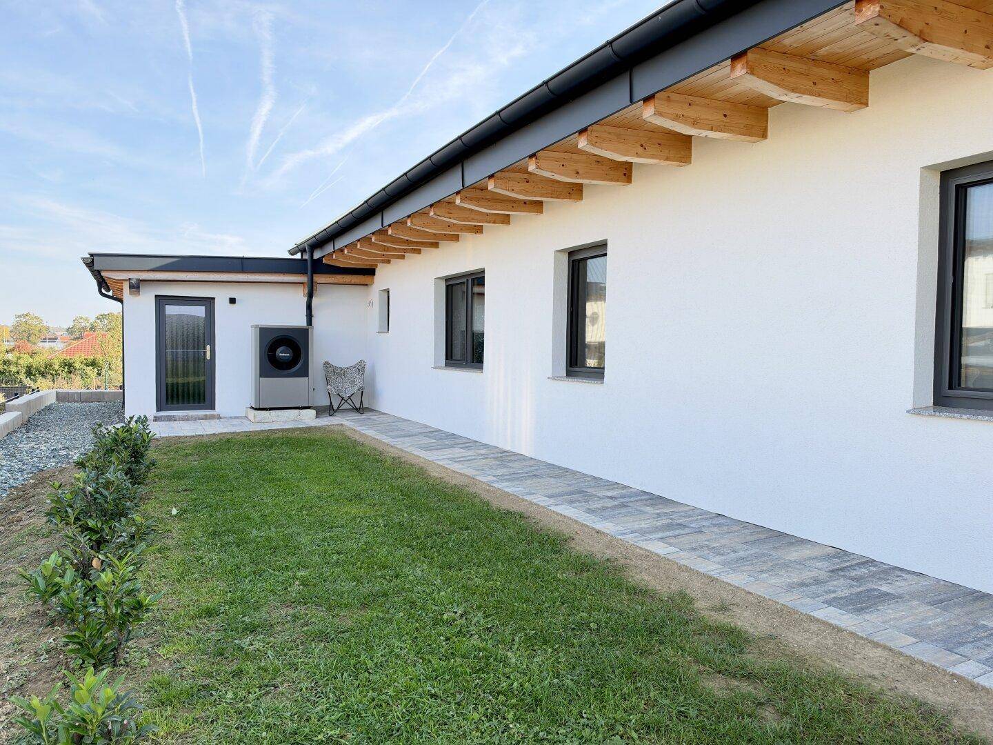 Seitenansicht des modernen Hauses mit Wärmepumpe und gepflegtem Gartenweg.