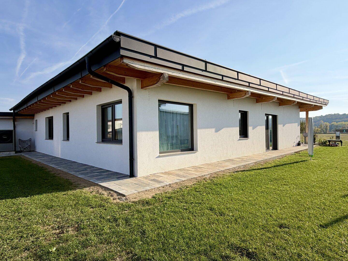 Modernes Einfamilienhaus mit weißer Fassade, dunklen Fenstern und weitläufigem Garten.