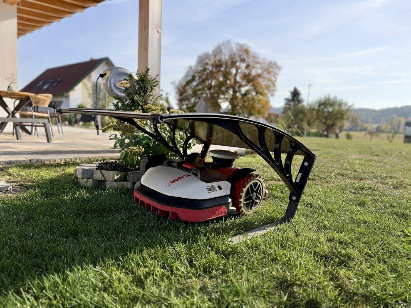 Gepflegter Gartenbereich mit Rasen und einem automatischen Rasenmäher unter einer Schutzhülle.