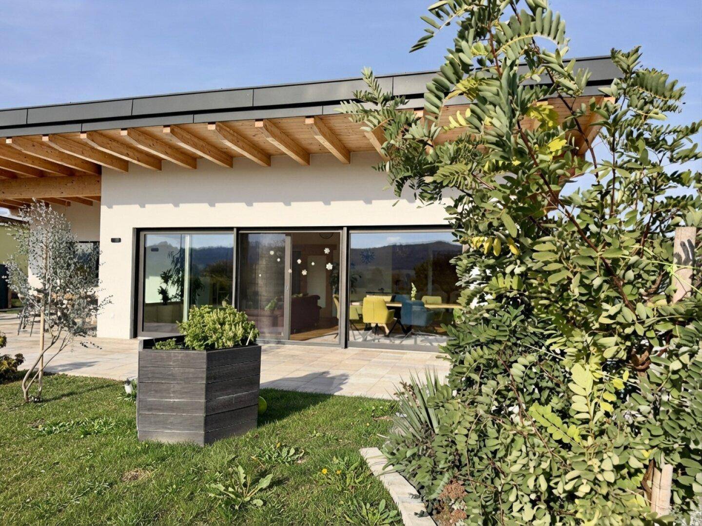 Moderne Hausfassade mit großen Schiebetüren und Blick auf den Garten und die Umgebung.