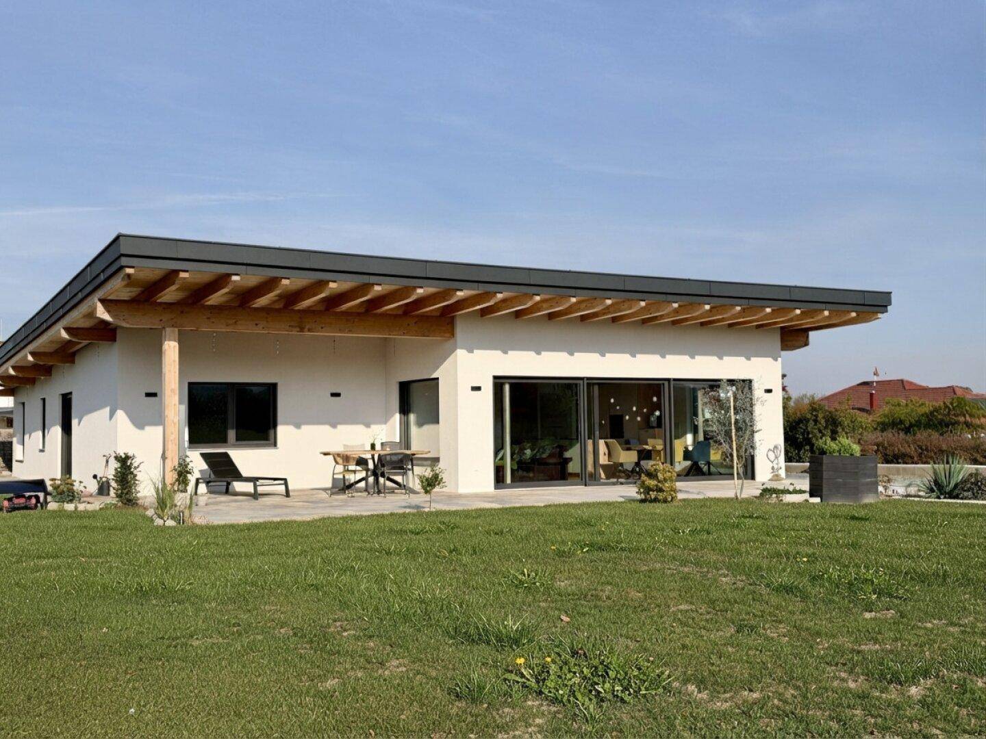 Modernes Einfamilienhaus mit Flachdach, Holzbalken und großer Rasenfläche.