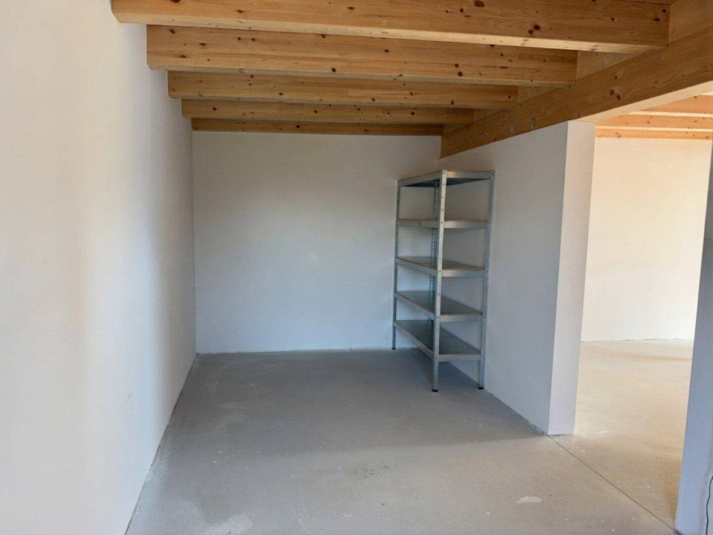 Praktischer Abstellraum mit Metallregal, Betonboden und Holzbalkendecke für zusätzlichen Stauraum.