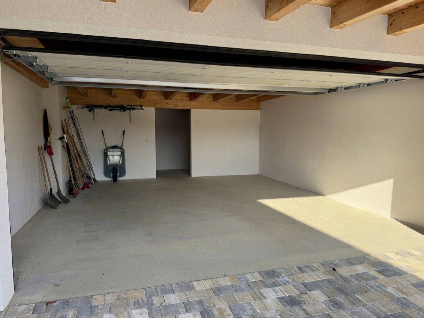 Geräumige Garage mit Betonboden, Holzbalkendecke und ausreichend Platz für Fahrzeuge und Lagerung.