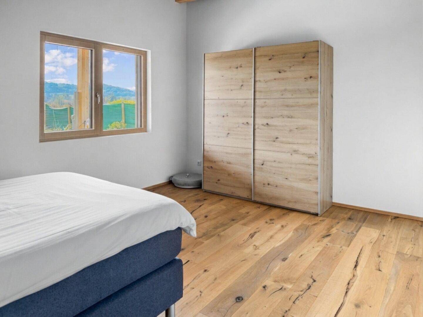 Schlafzimmer mit Holzboden, großem Kleiderschrank und Fenster mit grüner Aussicht.