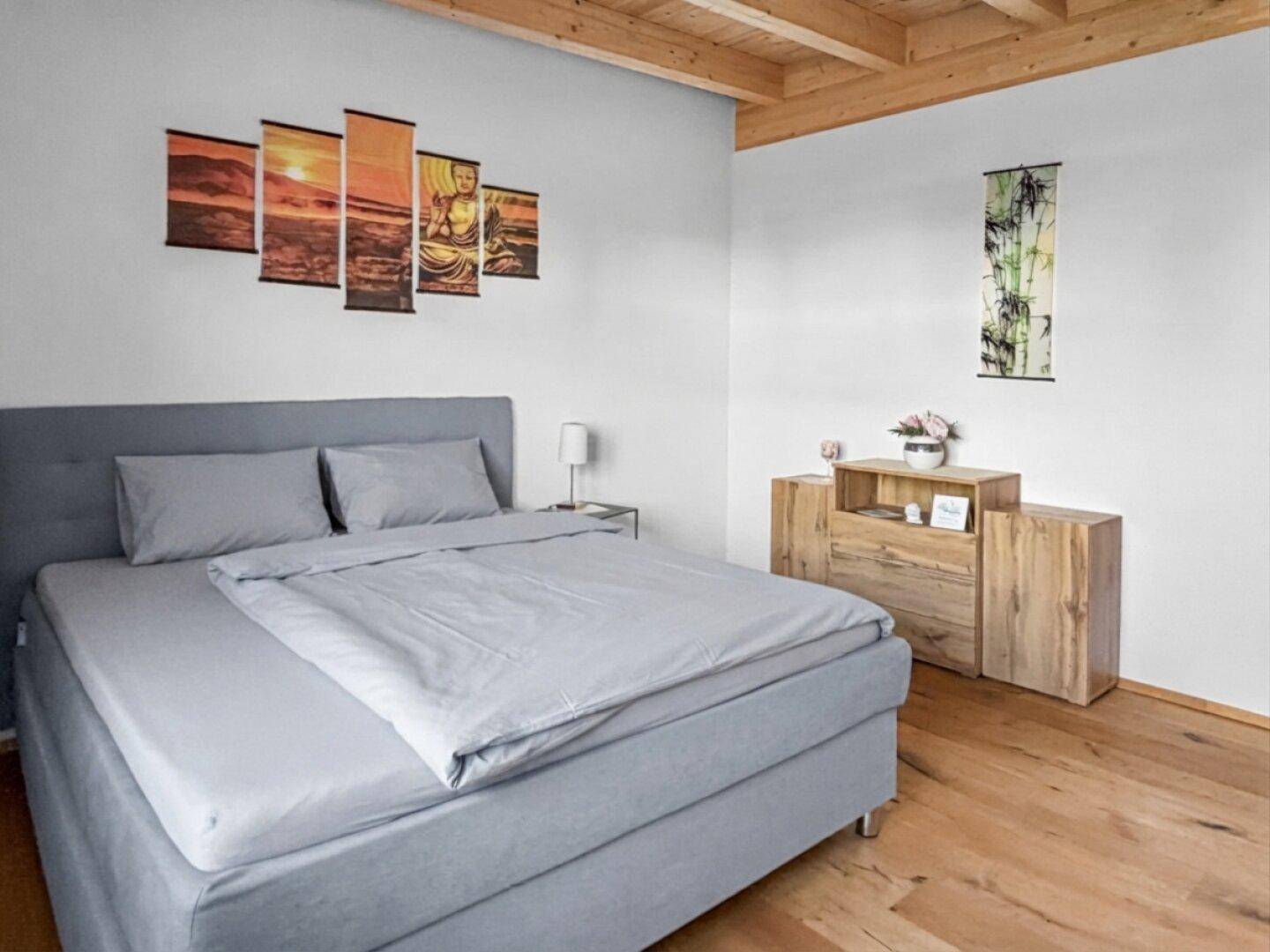 Helles Schlafzimmer mit grauem Bett, Holzboden und Holzmöbeln.
