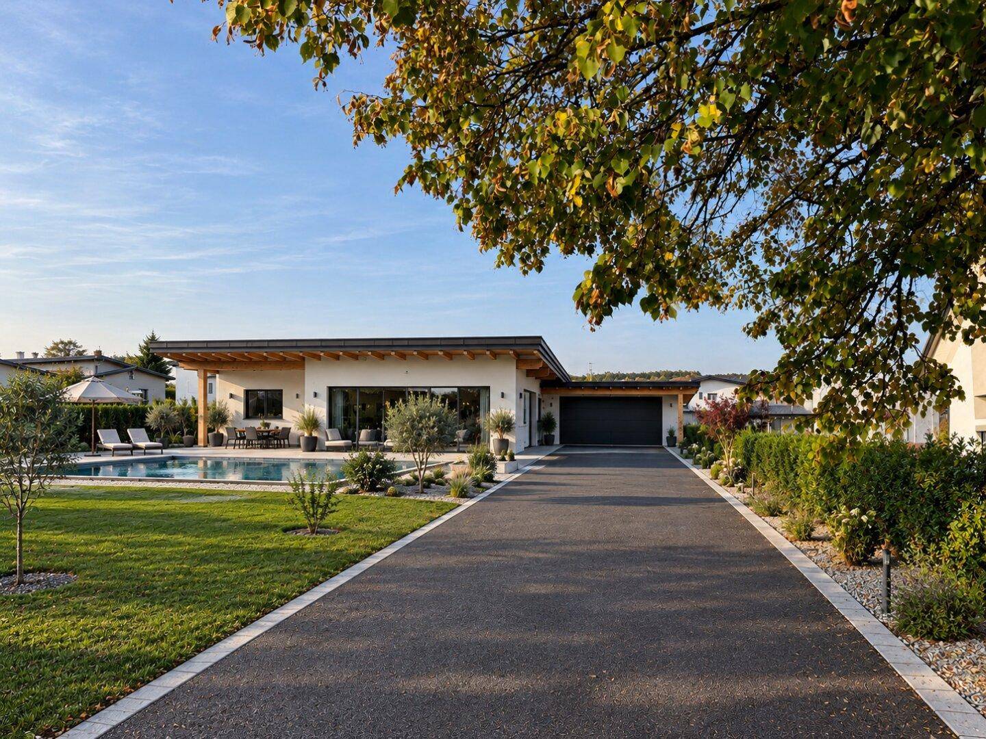 Moderne Villa mit weitläufiger Auffahrt, gepflegtem Garten und Swimmingpool unter blauem Himmel.