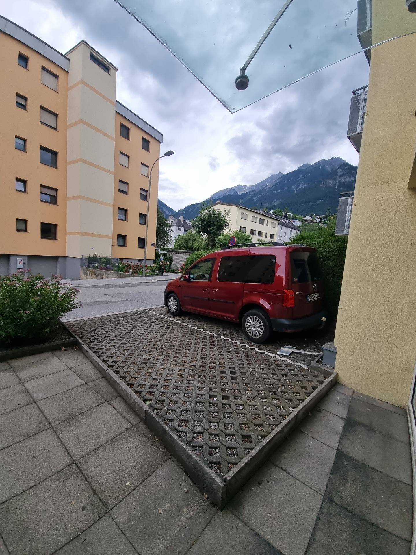 Außenansicht des Gebäudes mit Parkplatz, umgeben von weiteren Wohngebäuden und Bergen im Hintergrund.