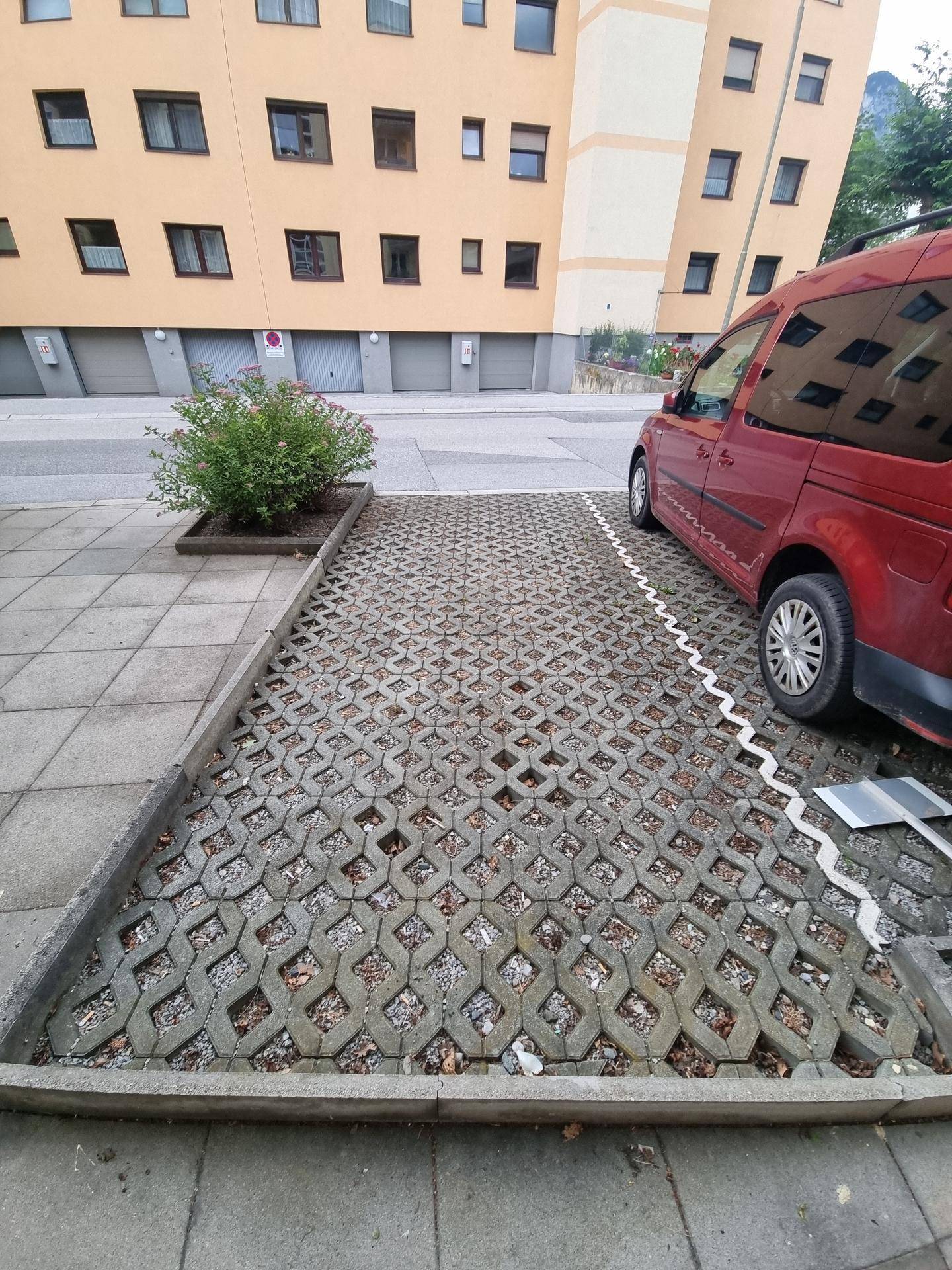 Detailansicht des gepflasterten Parkplatzes mit Rasengittersteinen vor der Gebäudefassade.