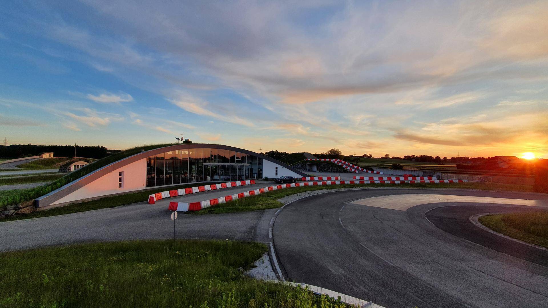 Modernes Gebäude mit begrüntem Dach und Teststrecke bei Sonnenuntergang, umgeben von Natur.