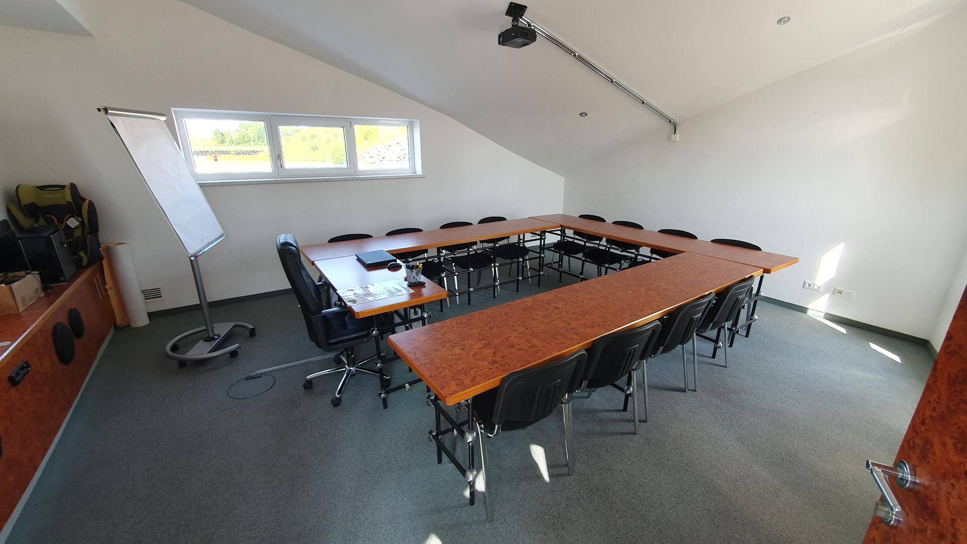 Funktionaler Konferenzraum mit U-förmiger Tischordnung, Beamer und Fenstern für Tageslicht.