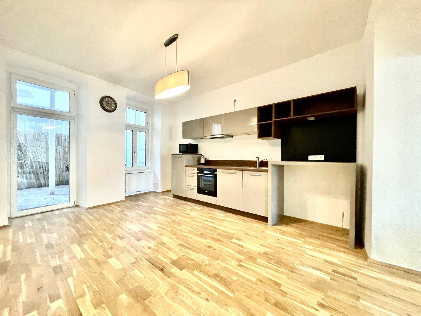 Helle Küche mit Parkettboden und Zugang zu einem Außenbereich durch eine Glastür.