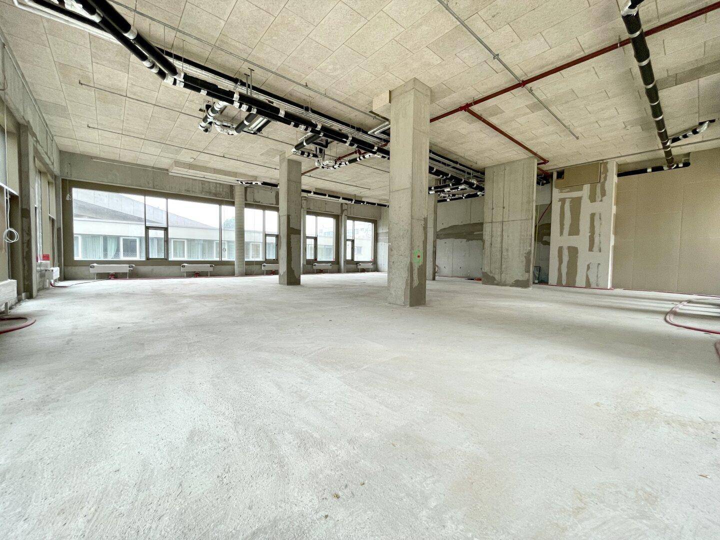 Heller Gewerberaum mit unverputzten Wänden, Betonboden und Deckeninstallationen.