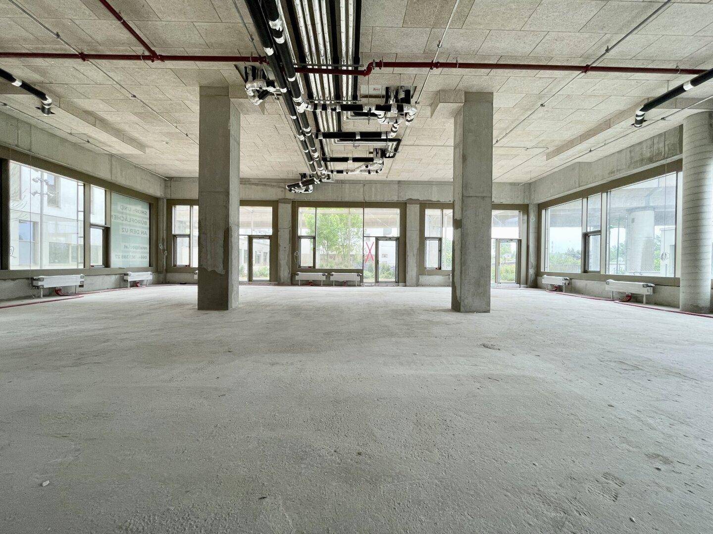 Geräumiger Gewerberaum mit Betonpfeilern, hohen Decken und viel Tageslicht durch die Fenster.
