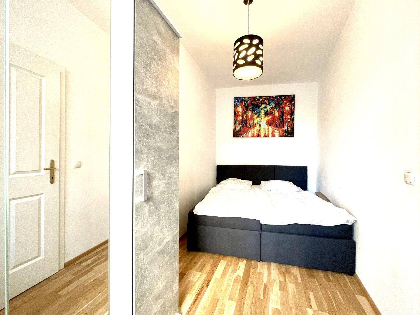 Schlafzimmer mit Doppelbett, Holzboden und einem farbenfrohen Kunstwerk an der Wand.