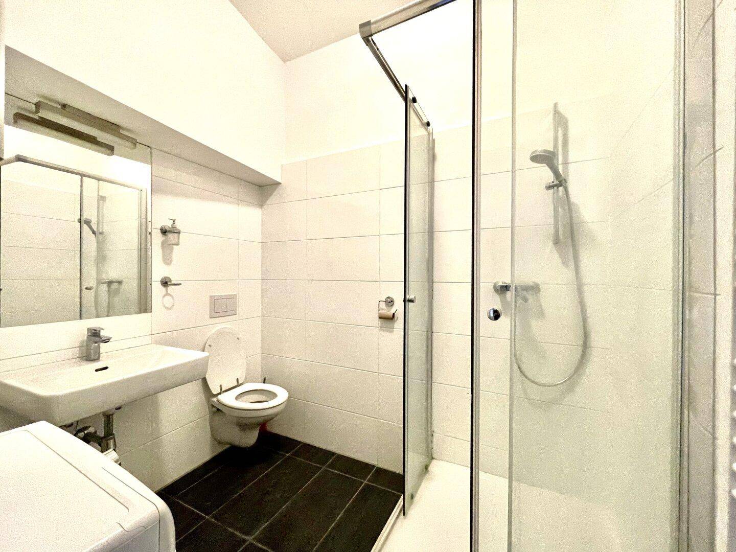 Modernes Badezimmer mit Duschkabine, WC und Waschbecken, ausgestattet mit weißen Fliesen.