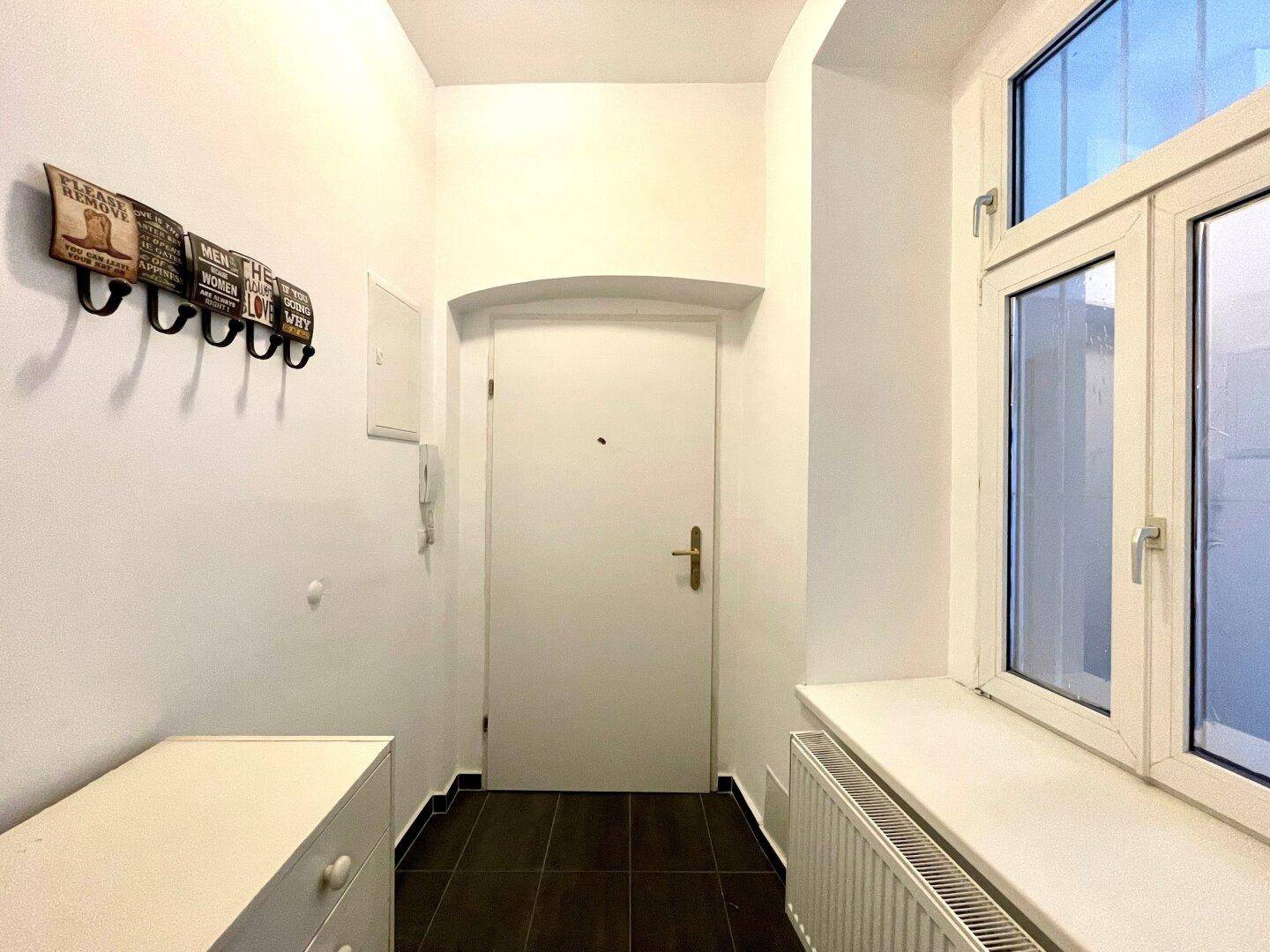 Heller Eingangsbereich mit Fenster, dunklen Fliesen und praktischen Garderobenhaken.
