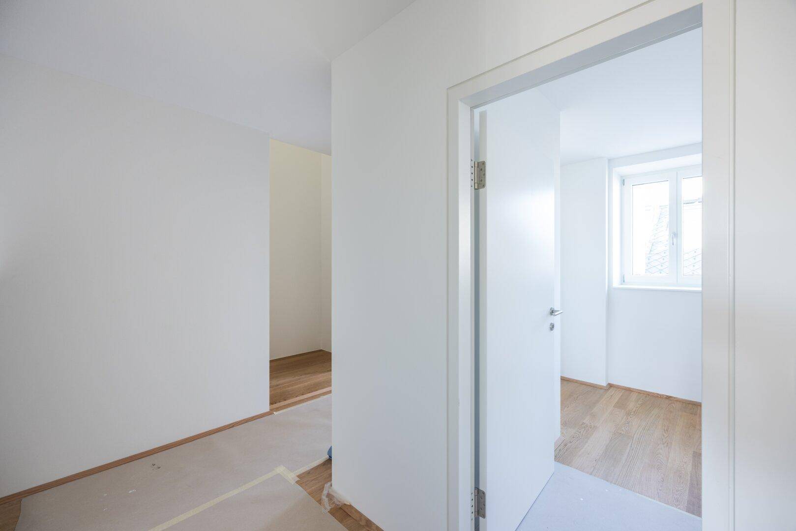 Heller Flur mit Holzboden, der zu einem weiteren Raum mit Fenster führt.