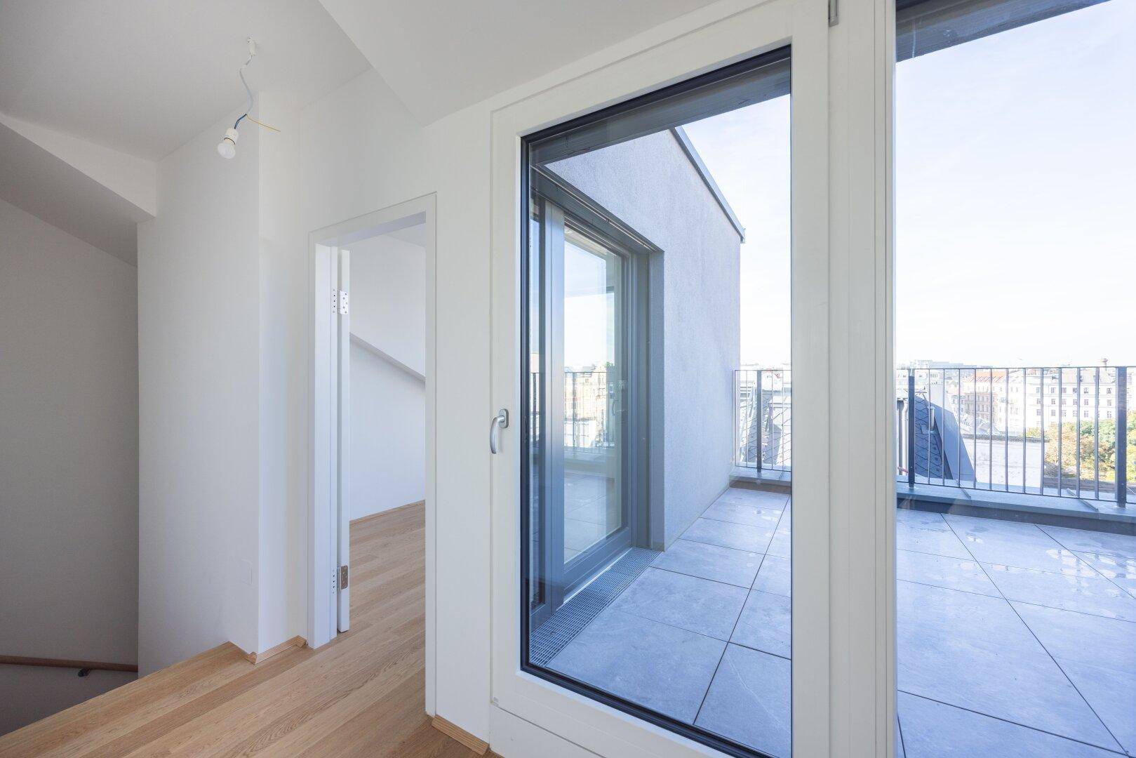 Heller Flur mit Holzboden und Zugang zu einer großen Dachterrasse mit Stadtblick.