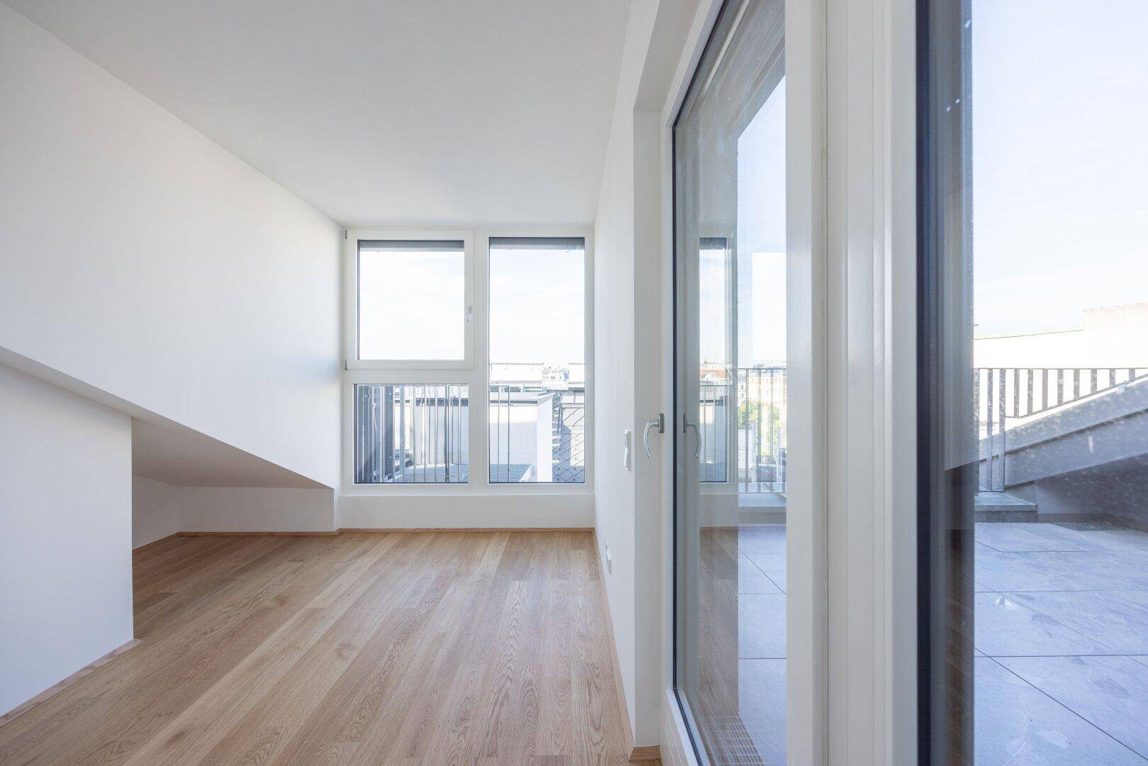 Heller Raum mit Holzboden und großen Fenstern, die einen weiten Blick über die Stadt bieten.