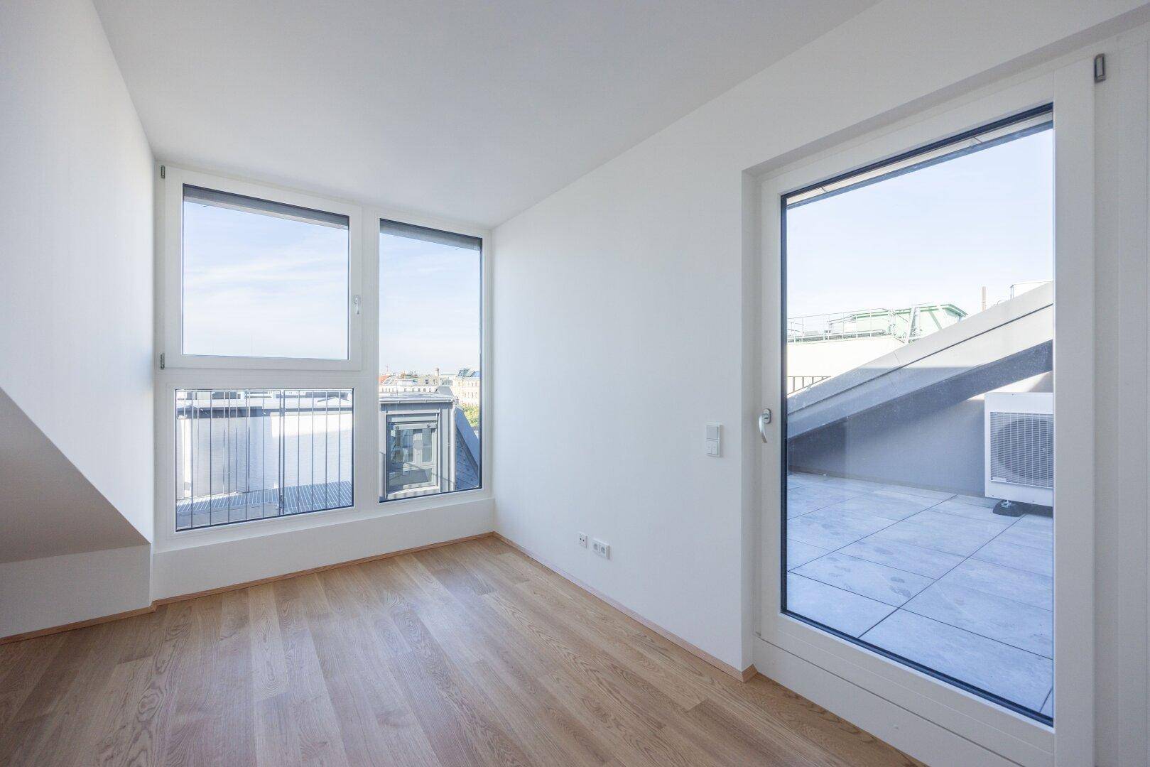 Geräumiger Raum mit Holzboden und Zugang zu einer Dachterrasse, ideal für ein Arbeitszimmer.