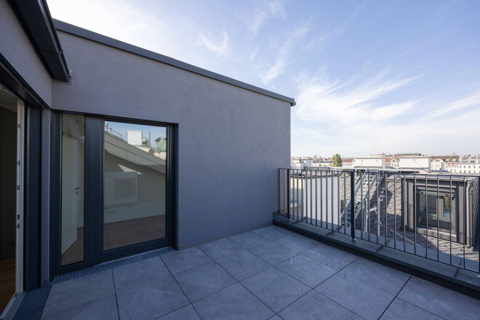 Geräumige Dachterrasse mit Fliesenboden und Blick über die Dächer der Stadt.