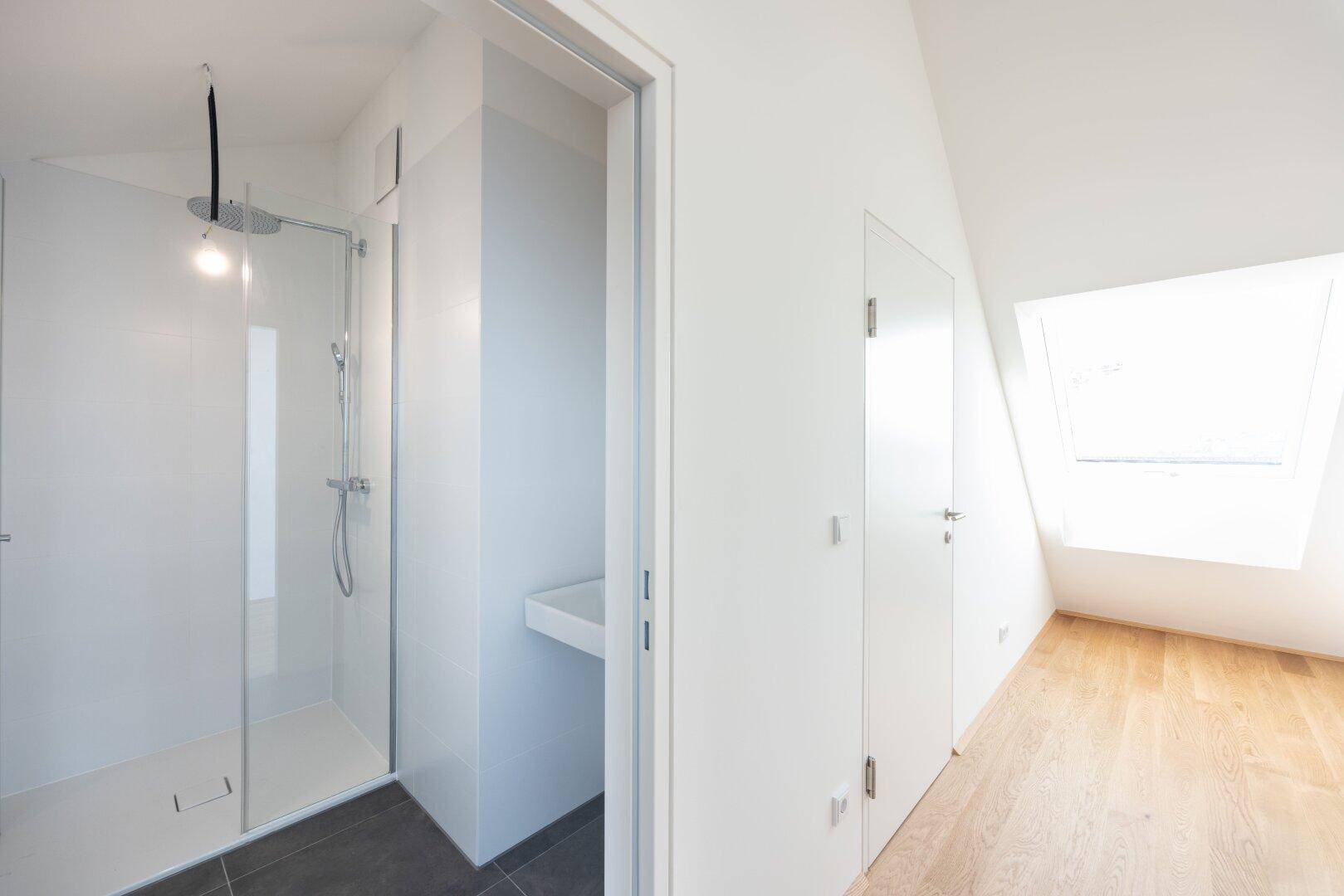 Modernes Badezimmer mit begehbarer Dusche und Dachfenster, angrenzend an einen hellen Raum.