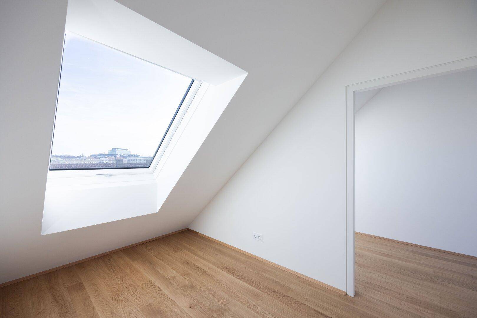 Heller Dachgeschossraum mit Holzboden und großem Dachfenster, ideal für ein Schlafzimmer oder Büro.