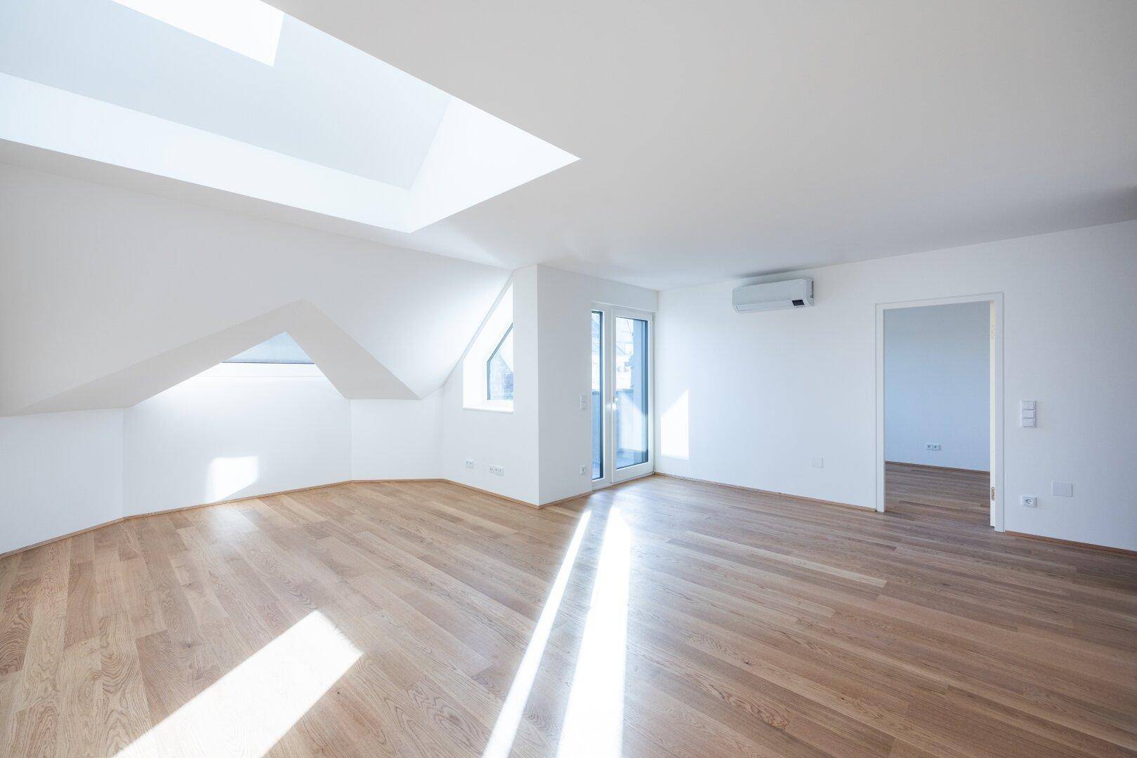 Geräumiger, heller Raum mit Holzboden, Dachfenstern und direktem Zugang zu einer Außenterrasse.