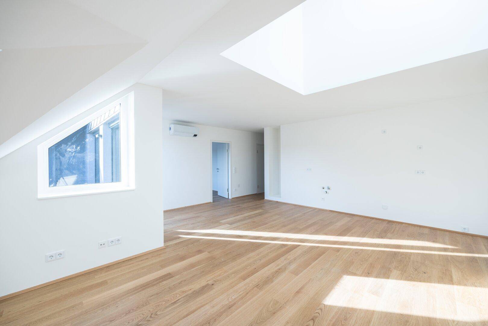 Heller Raum mit Holzboden, Klimaanlage und schrägem Dachfenster, bereit für die Einrichtung.