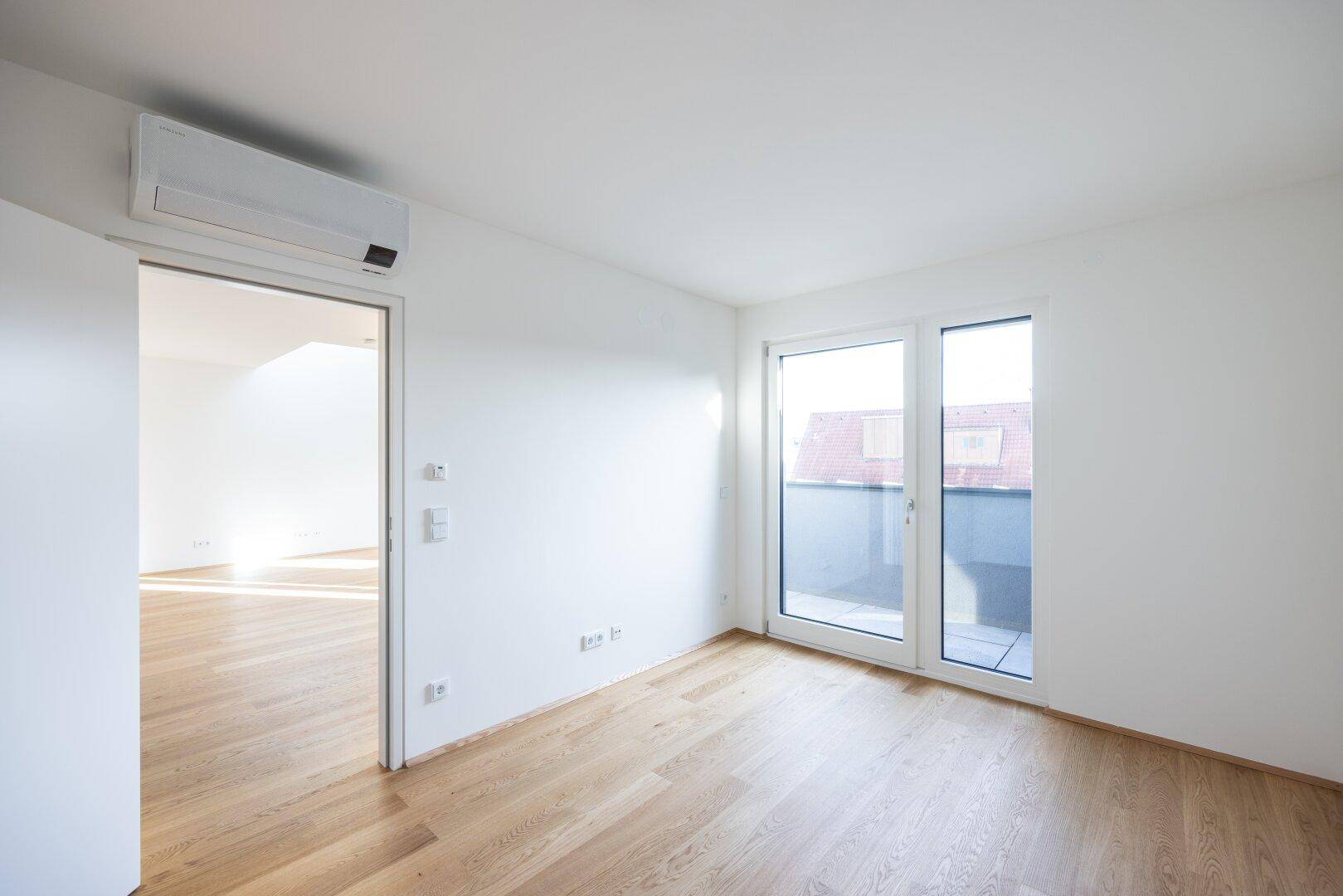 Heller Raum mit Holzboden, Klimaanlage und Terrassentür, ideal als Schlaf- oder Arbeitszimmer.