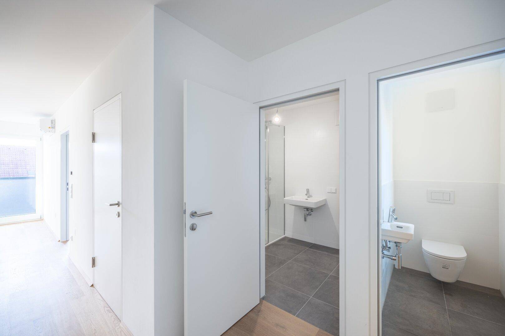 Heller Flur mit Holzboden, der zu einem modernen Badezimmer und einer separaten Toilette führt.
