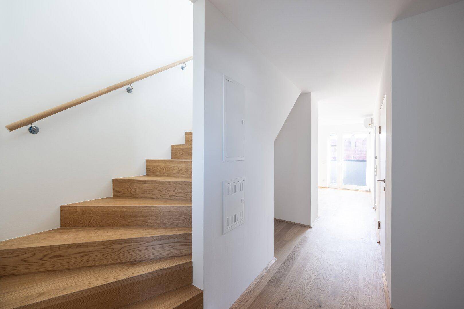 Heller Flur mit Holztreppe und modernem Geländer, führt zu den oberen Etagen.