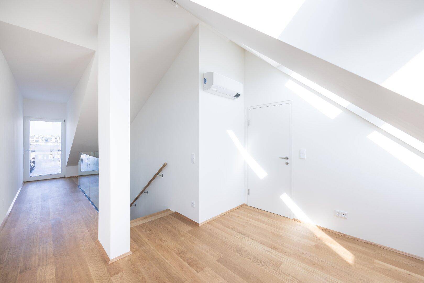 Heller Flur im Dachgeschoss mit Holzboden, Klimaanlage und Zugang zu weiteren Räumen.