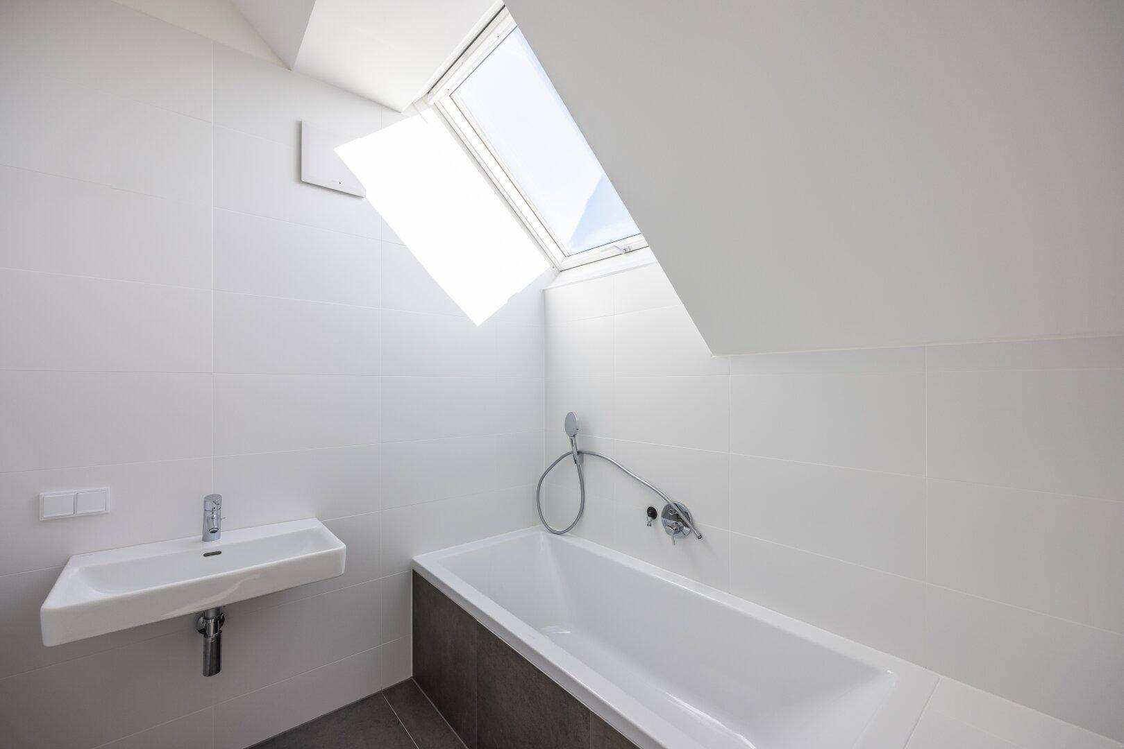 Modernes Badezimmer mit Badewanne, Einzelwaschbecken und Dachfenster für natürliches Licht.
